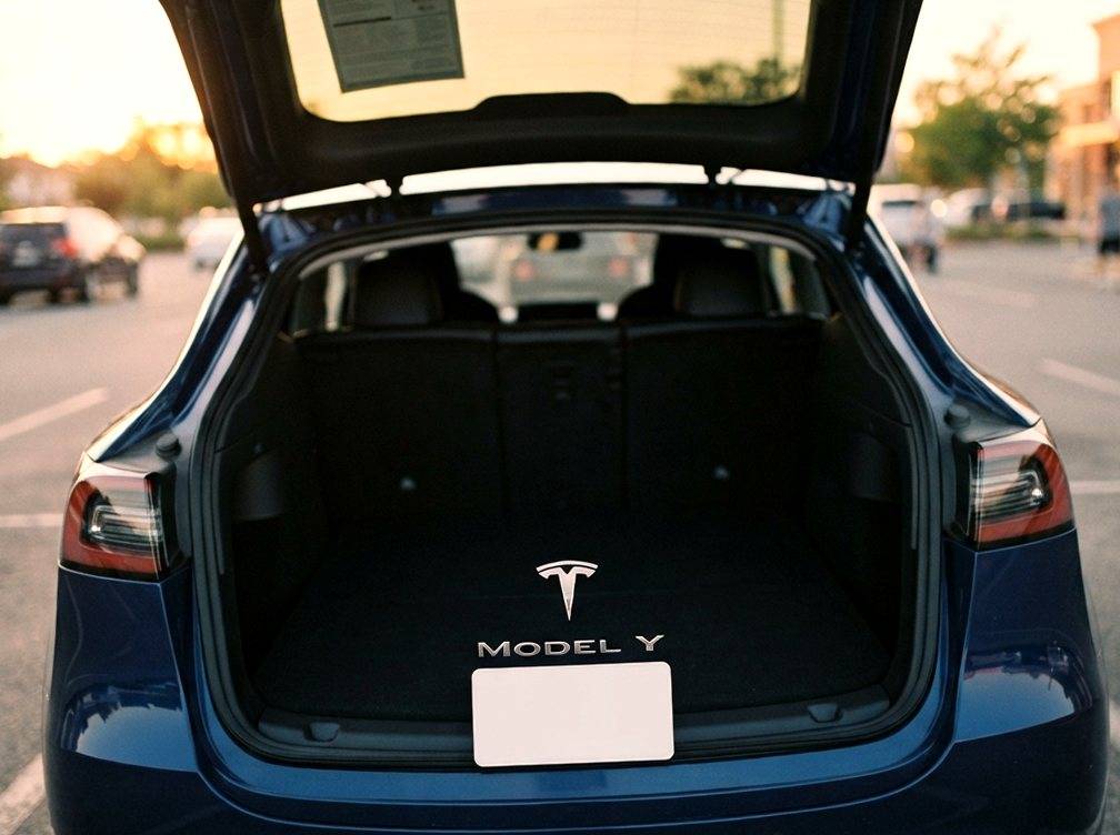 A price sticker is visible on the window of a Tesla Model Y L parked in a dealership showroom.